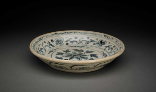 A shallow, off-white ceramic dish featuring dark blue painted floral designs. The interior displays a central flower surrounded by a continuous band of scrolling vines and smaller blossoms.