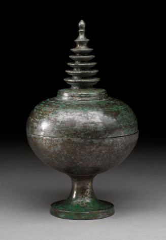The domed cover has a raised central section surmounted by a five-storied stupa with a bud-shaped finial over two knobs; the cover is incised with bands of fine lines; the cup is on a waisted stem with a widely spread foot