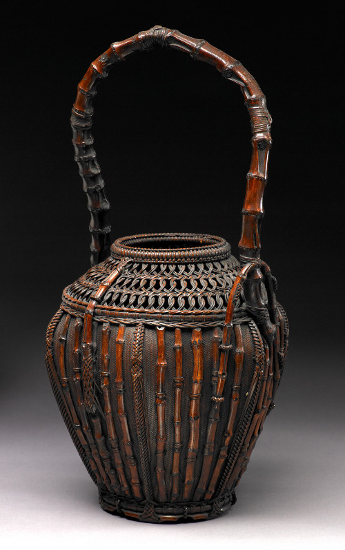 A karamono style bamboo basket of hexagonal form with seven jewel design at neck, curved bamboo segment handle and intricate knots.
