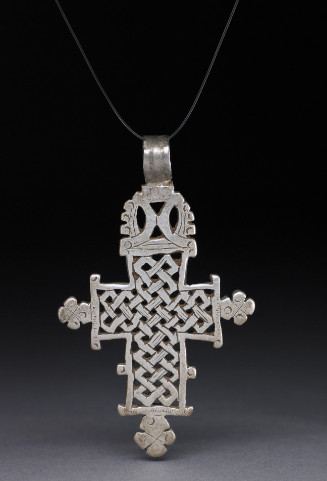 Silver pendant in the form of a Latin cross; ends of each arm have trefoil shaped finials; cross has a thick silver border enclosing an interlace and loop pattern with pierced square shapes; the superior arm has an intricate decorative finial with a ring for suspension attached
