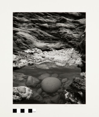A black and white photograph of a nature scene looking down at rocks and a clear body of water. 