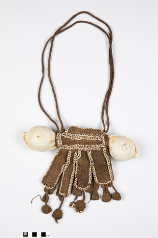 Plaited fiber in hanging rectangles edged with cowrie shells. Front has 4 hanging panels with attached dangling disc. Repeat in back. Large shells are mounted on either side of plaited fiber. Connected by stick that supports fiber. Double loops.