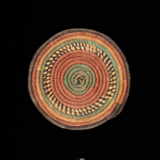Round disk made of green, tan and brown dyed fibers, coiled and sewn together.