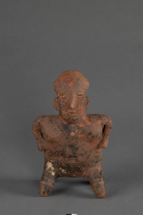 A mottled reddish-brown and black clay figurine with its hands resting on its hips. Standing on short, stubby legs, the figure features a bulbous head, large semi-circular ears, narrow slit eyes, and a prominent nose.






