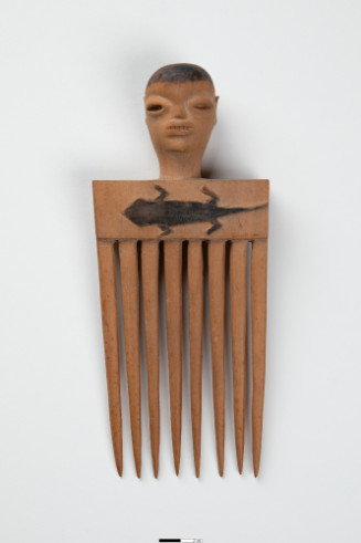 Wooden comb with 8 teeth with relief image of lizard on shaft surmounted by carving of a man’s head.